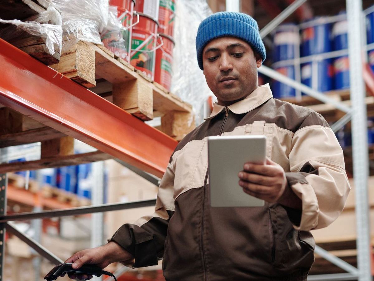 Warehouse worker reading a tablet while scanning stock on a rack of drums