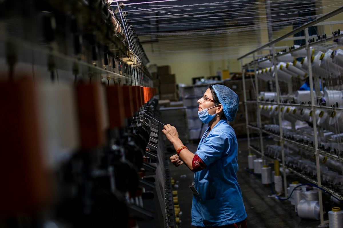 Operator pabrik tekstil memeriksa benang pada mesin pemintal